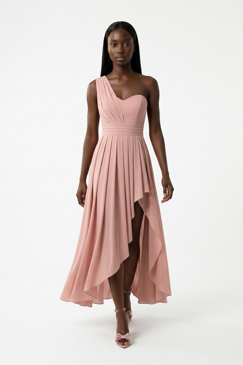 A model wearing a dusty pink one-shoulder midi dress with a pleated skirt and high-low hemline, standing against a plain white studio background.