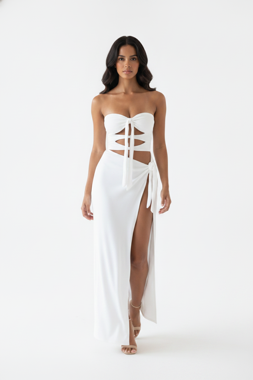 A woman modeling a strapless white maxi dress with a corset-style lace-up bodice, side cutouts, and a high slit, photographed against a plain white studio background.