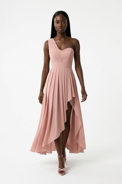 A model wearing a dusty pink one-shoulder midi dress with a pleated skirt and high-low hemline, standing against a plain white studio background.