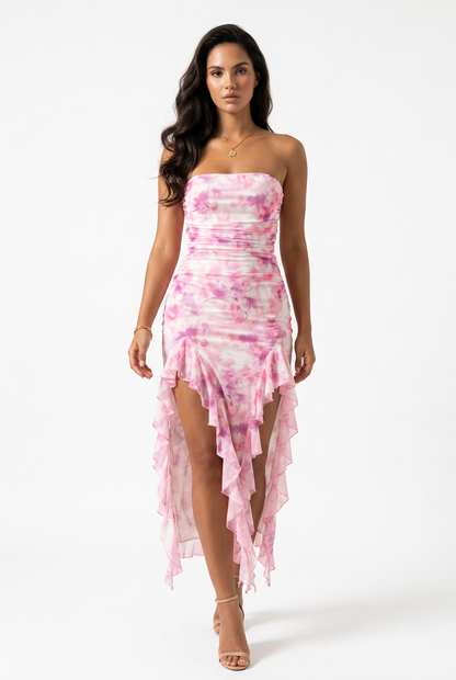 A woman models a strapless high-low dress with a pink and white tie-dye floral pattern, set against a plain white studio background.