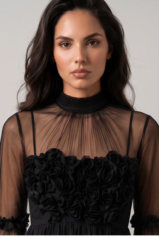 A woman wearing a black sheer mesh mock-neck top with long sleeves and a black ruffled rose-patterned bodice, photographed against a plain light gray studio background.