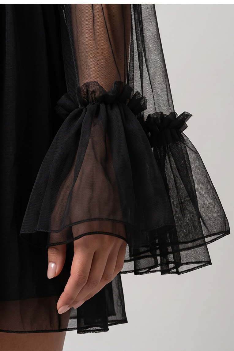 Close-up of a person wearing a black sheer tulle dress with dramatic ruffled bell sleeves and gathered cuffs, shown against a light neutral background.