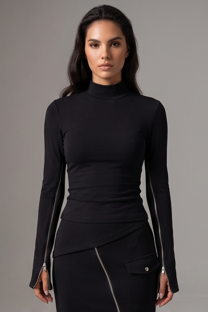 A woman modeling a fitted black long-sleeve mock neck top with silver zipper details running down the sleeves and at the hem, paired with a matching black skirt, against a solid gray studio background.