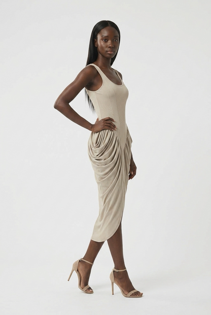 A model wearing a sleeveless, draped midi dress in a light beige color, paired with beige high-heeled sandals, posed against a solid white studio background.