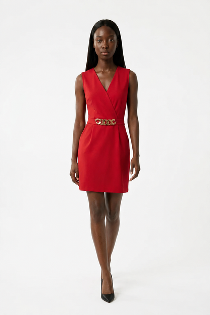 A model wearing a sleeveless red wrap-style mini dress with a gold chain-link belt at the waist, paired with black pointed-toe heels, against a plain white studio background.