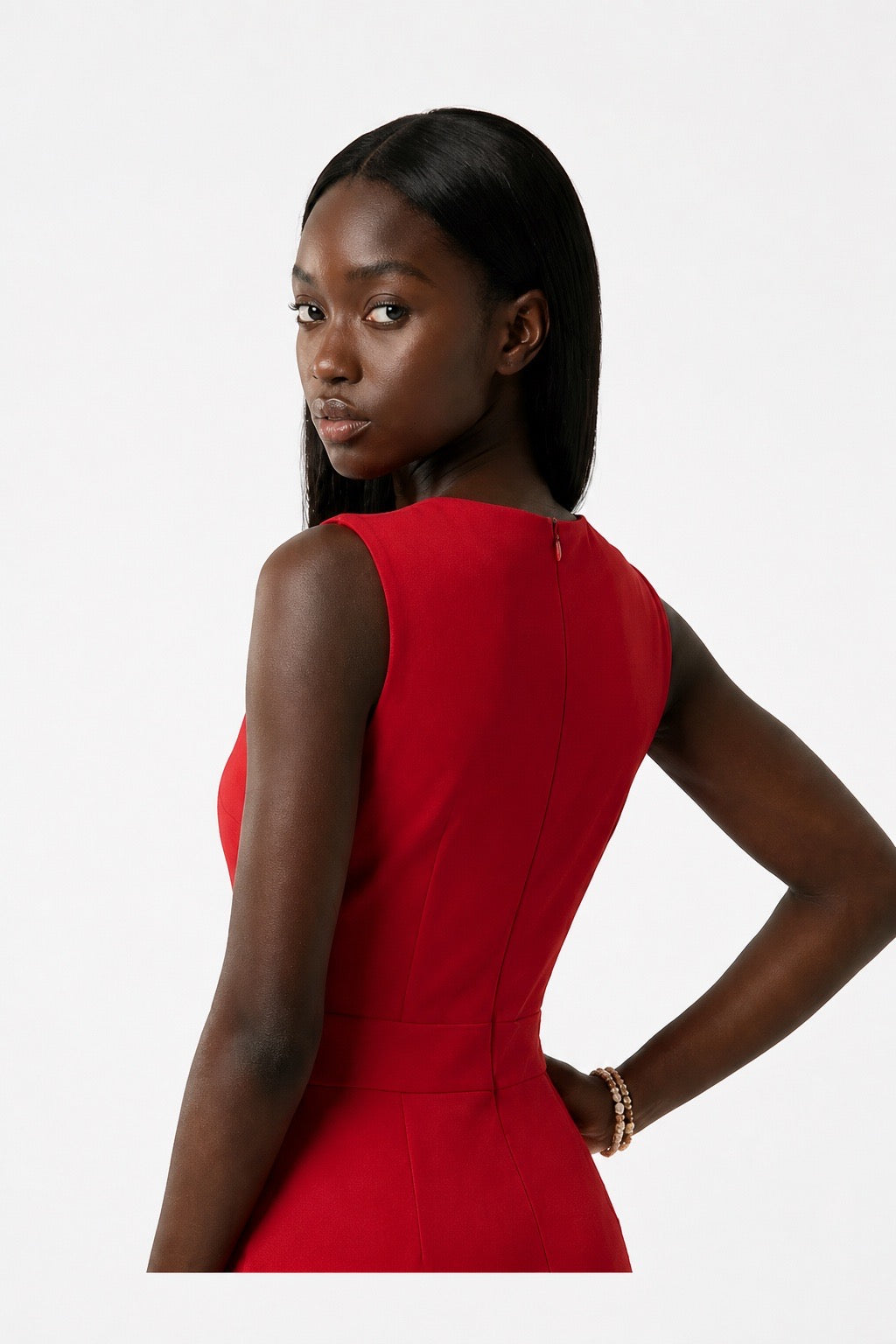 A woman modeling a sleeveless red dress from the back, showing a structured waist seam, against a plain light gray studio background.