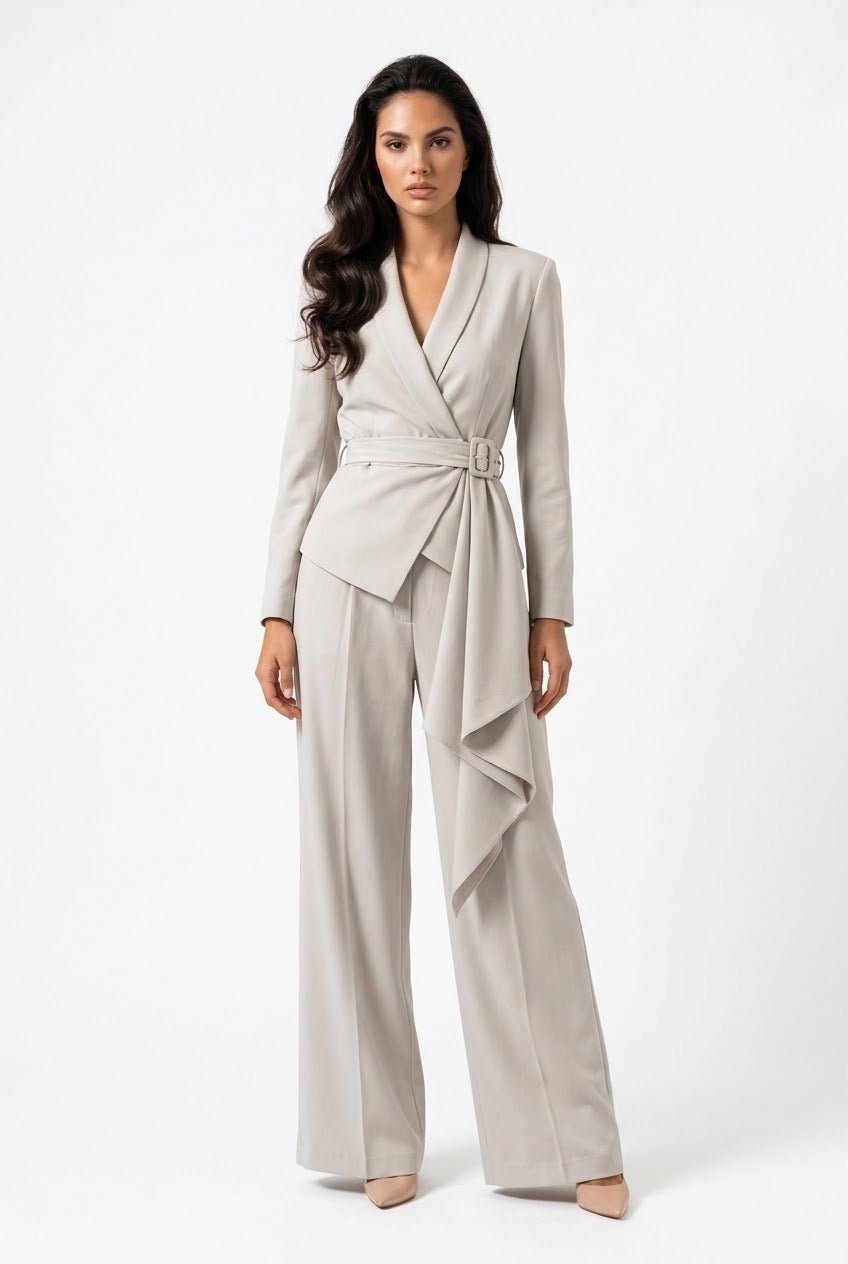 A woman modeling a light beige wrap-style blazer with a matching waist tie and wide-leg trousers, photographed against a plain white studio background.